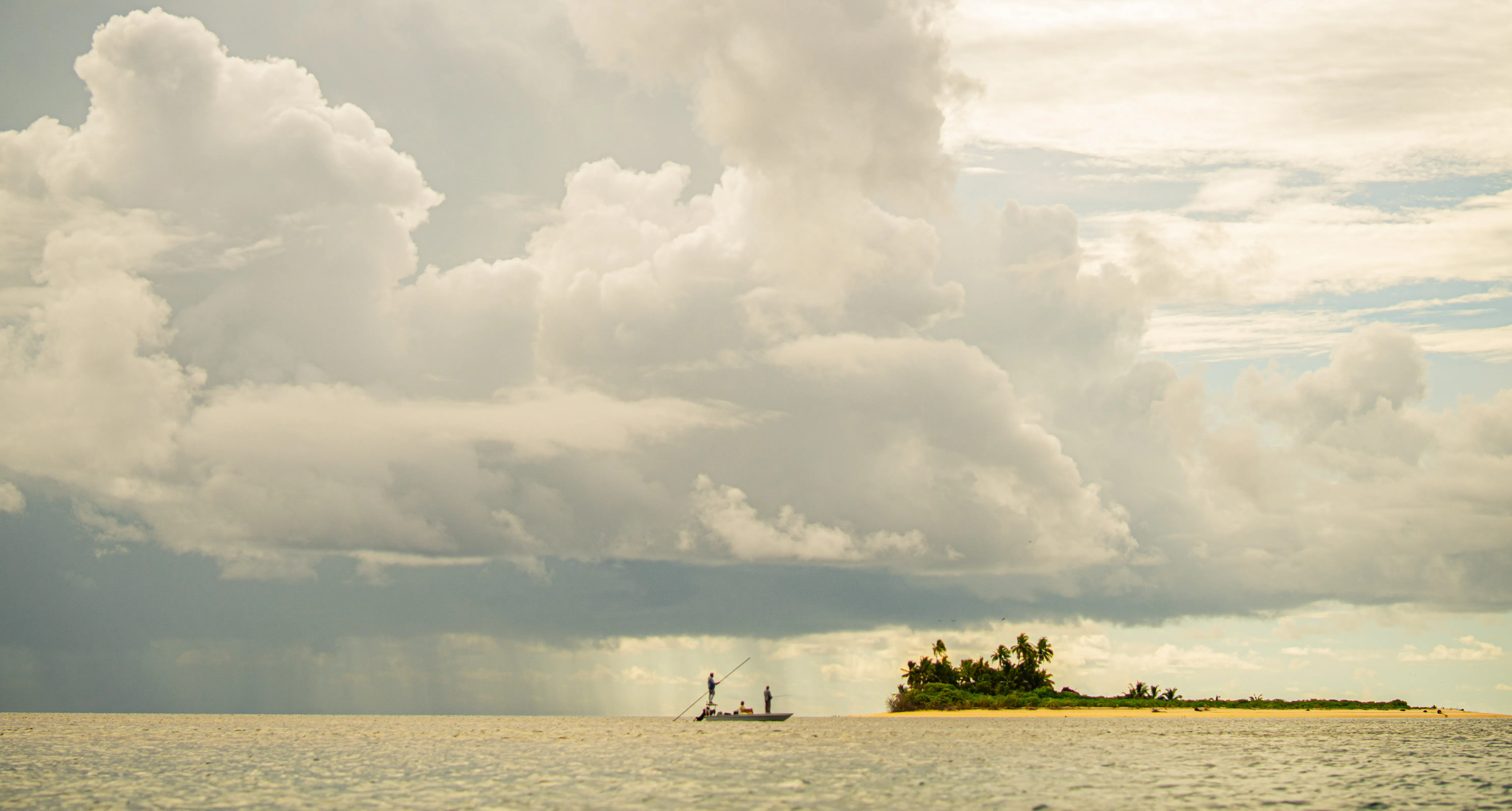 Skiff and small island under towering clouds at St Francois Atoll